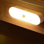 Oval LED motion sensor night light glowing warm on a wood wall