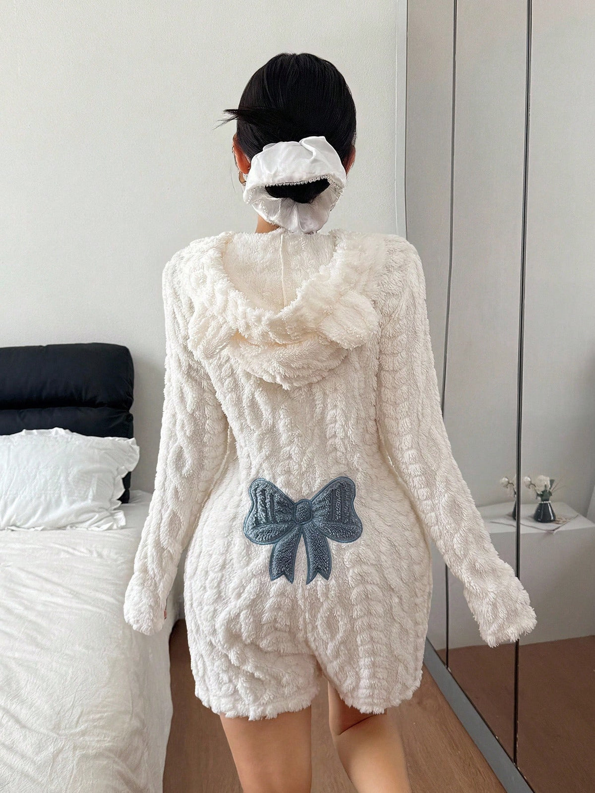 Back of a white plush hooded romper with a raised cable-style texture and a blue bow