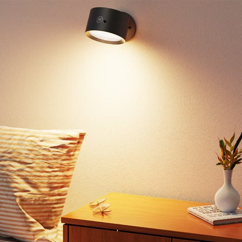 Black round wall light glowing warm white over a bed and wooden nightstand
