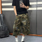 Model in a black tee and camo patchwork denim cargo shorts taking a mirror photo, hem below the knee