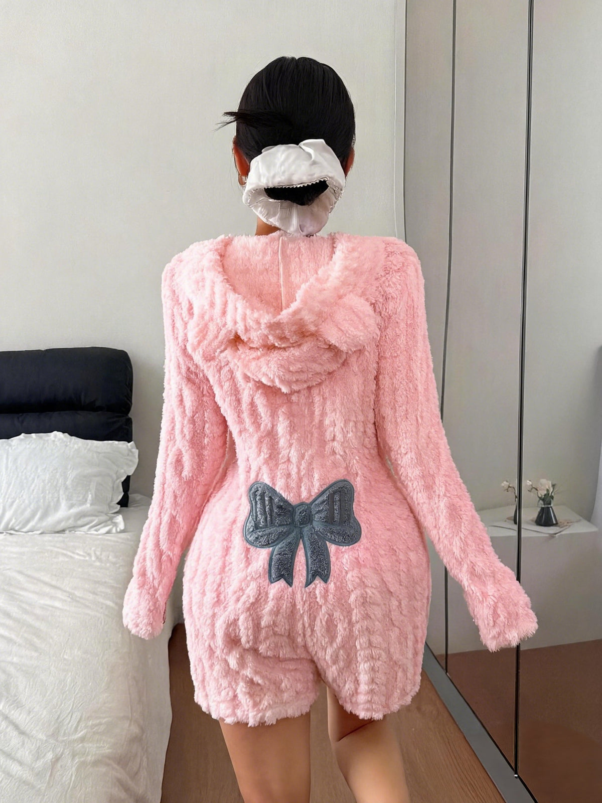 Back of a pink plush hooded romper with a raised cable-style texture and a blue bow