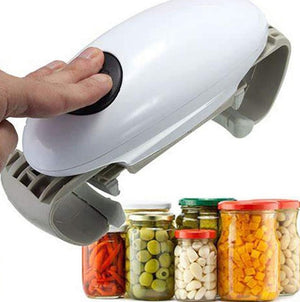 A hand holds a white electric jar opener above a row of pickle, olive, garlic and corn jars