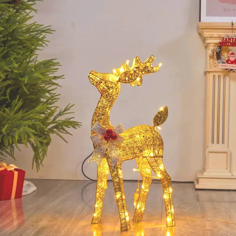 Golden lit reindeer with a silver bow looking up beside a fireplace and green branches