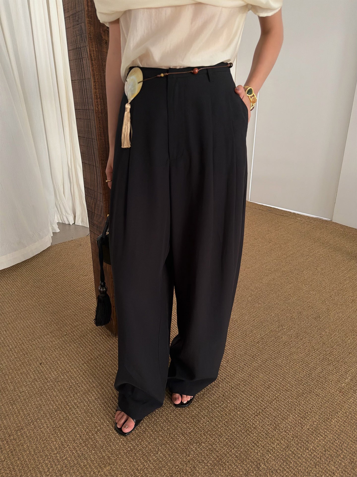 Black high waist wide leg trousers worn with a cream top and belt, side pocket view