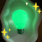 Bulb squeeze toy glowing green on a pale surface in the dark, even light across the body