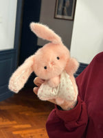 Pink squishy bean bag plush bunny toy held in one hand, floral cotton apron and long soft ears