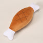 Brown plush chicken leg dog toy with stitched grill pattern and white bone ends on a cream background