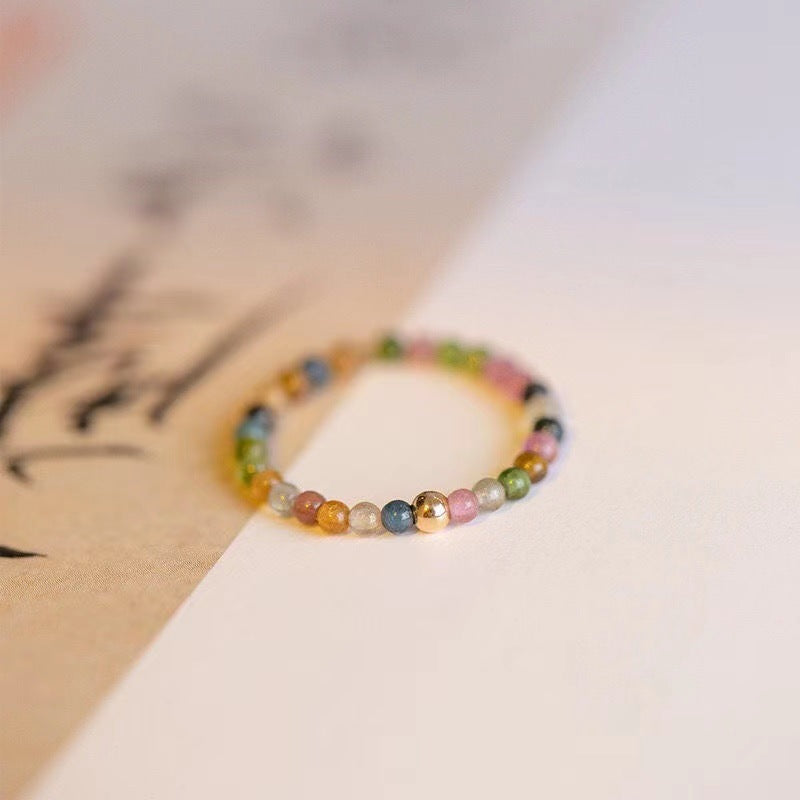 Rainbow tourmaline stretch ring worn on a finger, settled at the base