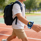 Child with a backpack walking on a track wearing a blue smart watch on the wrist