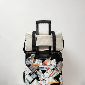 White gym bag with black handles sitting on a suitcase trolley handle through its back sleeve