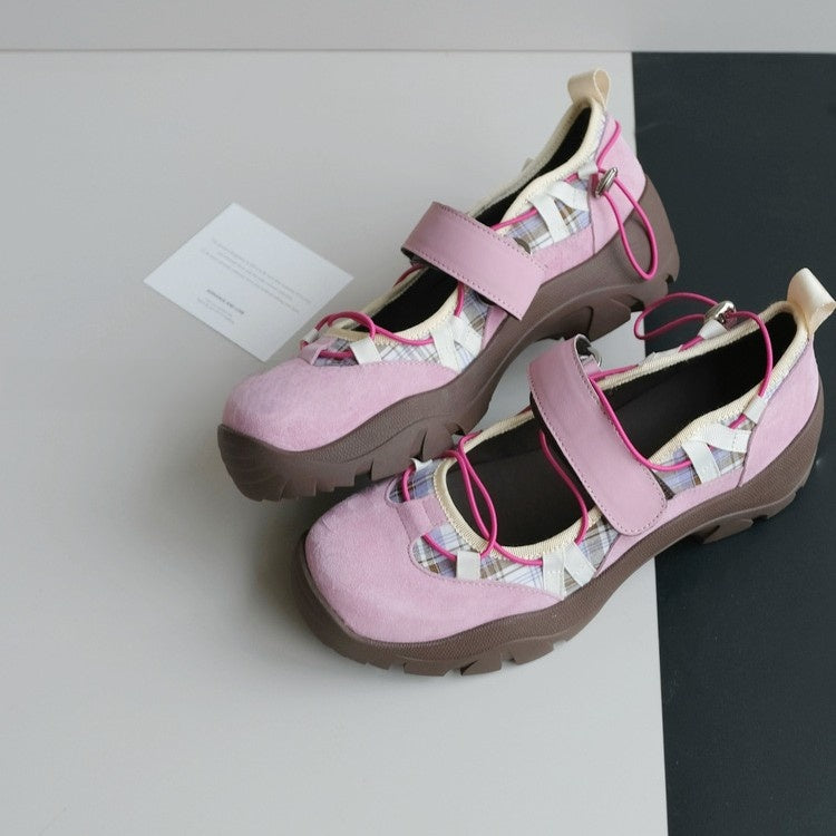 Pair of pink platform shoes with a wide strap, fuchsia elastic cords and a brown lug sole on a grey and black surface