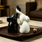 Couple elephant figurines on a leather tray, matte black and white with trunks curled together