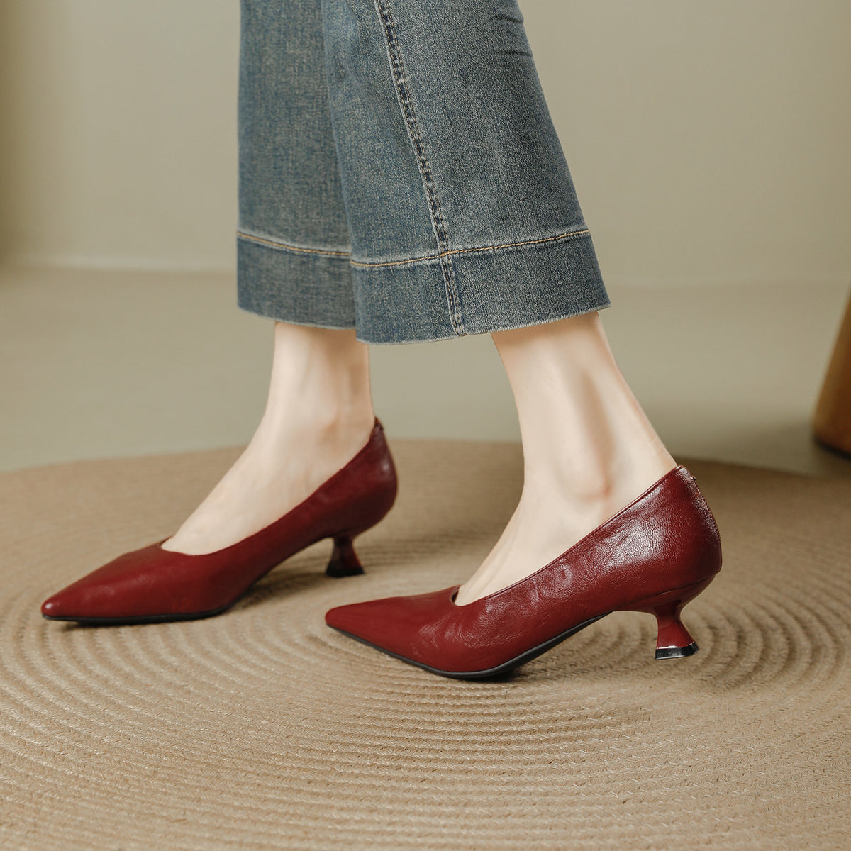 Burgundy pointed toe pumps with a low flared heel worn with cropped jeans on a woven rug