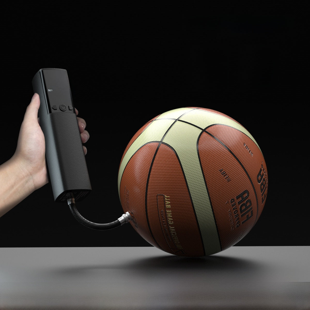 Black cordless handheld air pump inflating a basketball through its hose, held in a hand