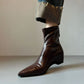 Dark brown pointed toe ankle boot with a wedge heel worn under rolled jeans