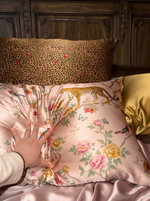 Pink floral and leopard print silk pillowcases layered on a bed with a hand pressing the fabric