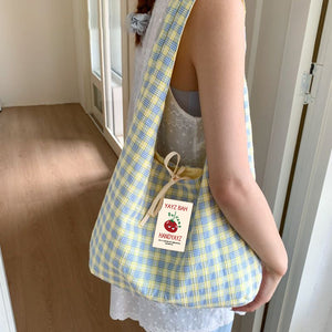 Pink and green plaid canvas single strap shoulder bag on a wooden floor