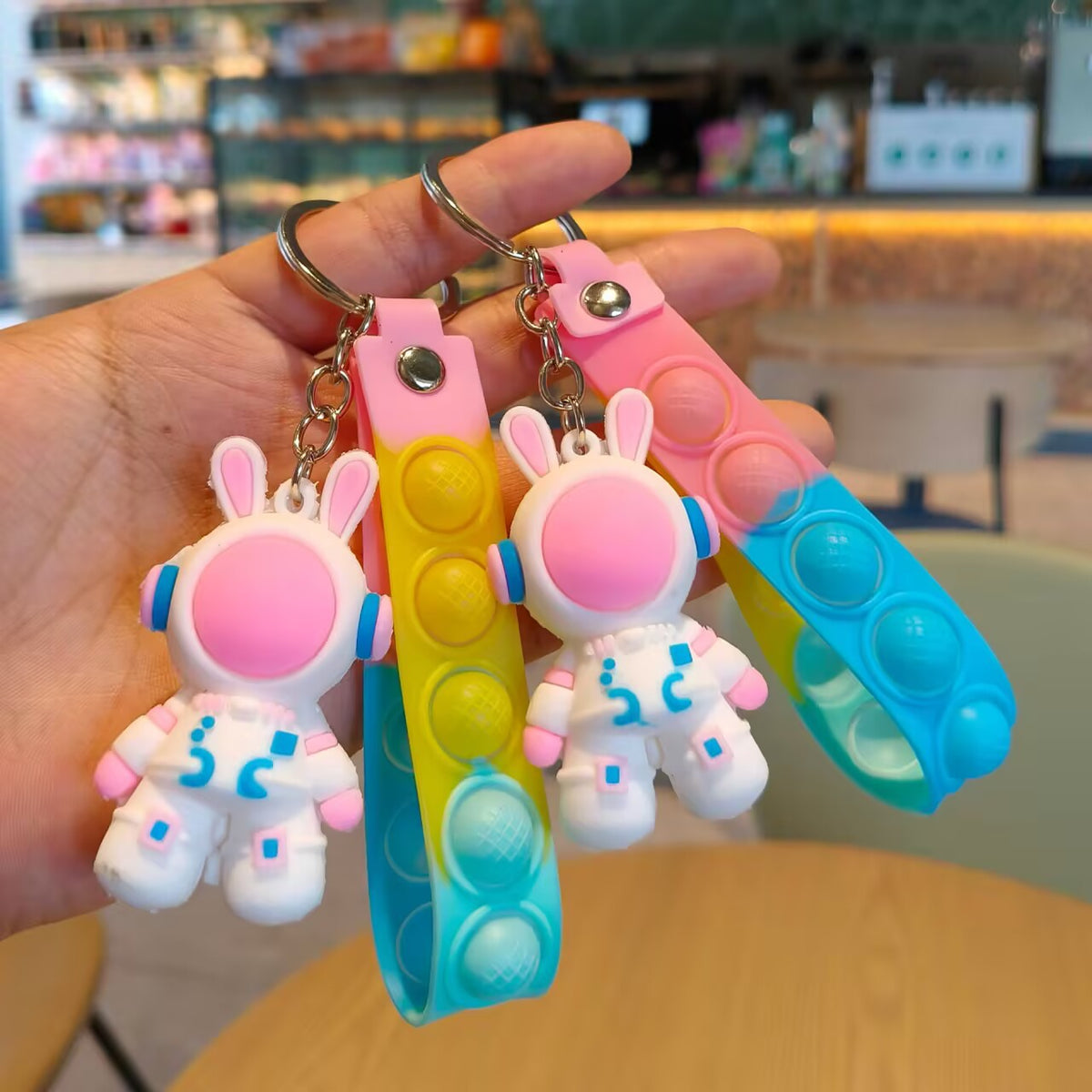 Pink helmet astronaut rabbit keychains on yellow and blue gradient silicone push pop straps in hand