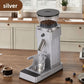 Silver electric coffee grinder beside espresso cup and scattered roasted coffee beans