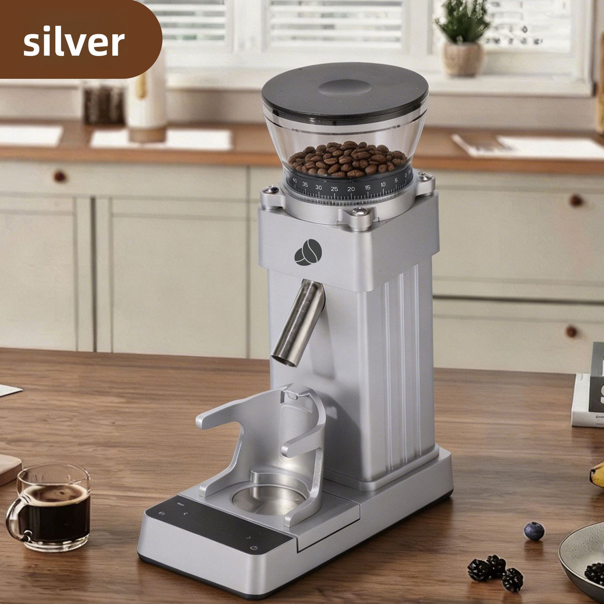 Silver electric coffee grinder beside espresso cup and scattered roasted coffee beans