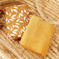 Two folded cotton muslin baby blankets, one mustard botanical print and one solid mustard, in a basket