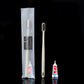 Beige straw toothbrush with charcoal bristles, toothpaste tube and frosted pouch on a black ground