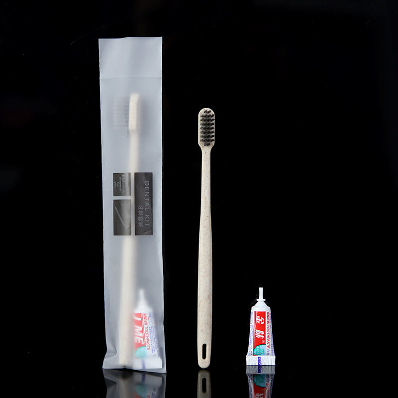 Beige straw toothbrush with charcoal bristles, toothpaste tube and frosted pouch on a black ground