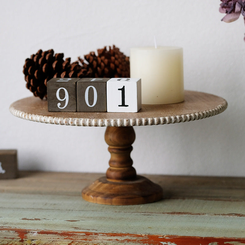 Wooden cake stand styled with a pillar candle, pine cones and number blocks as decor