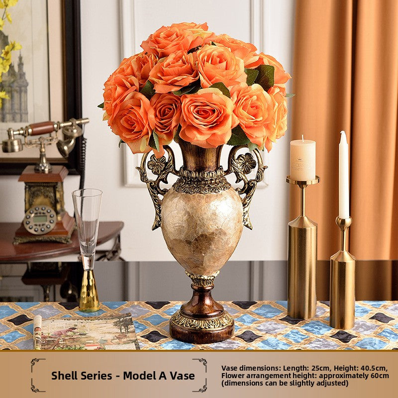 Tall resin vase with pearl shell body and gold tone handles holding an orange faux rose arrangement