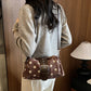 Woman wearing the brown polka dot shoulder bag with buckle band across the body over a gray sweater