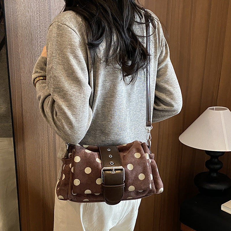 Woman wearing the brown polka dot shoulder bag with buckle band across the body over a gray sweater