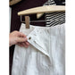Hand holding open the front fly of white linen shorts showing button hook and zip