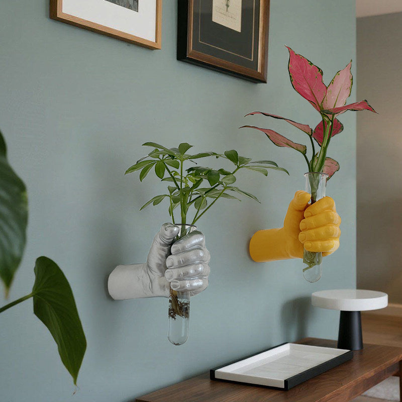 Silver and gold hand shaped wall vases holding glass tubes with leafy stems on a blue wall
