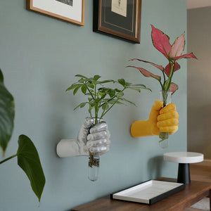 Silver and gold hand shaped wall vases holding glass tubes with leafy stems on a blue wall