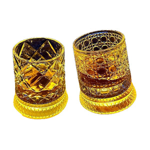 Two cut glass whiskey tumblers on white, diamond and hobnail facets lit amber at the base