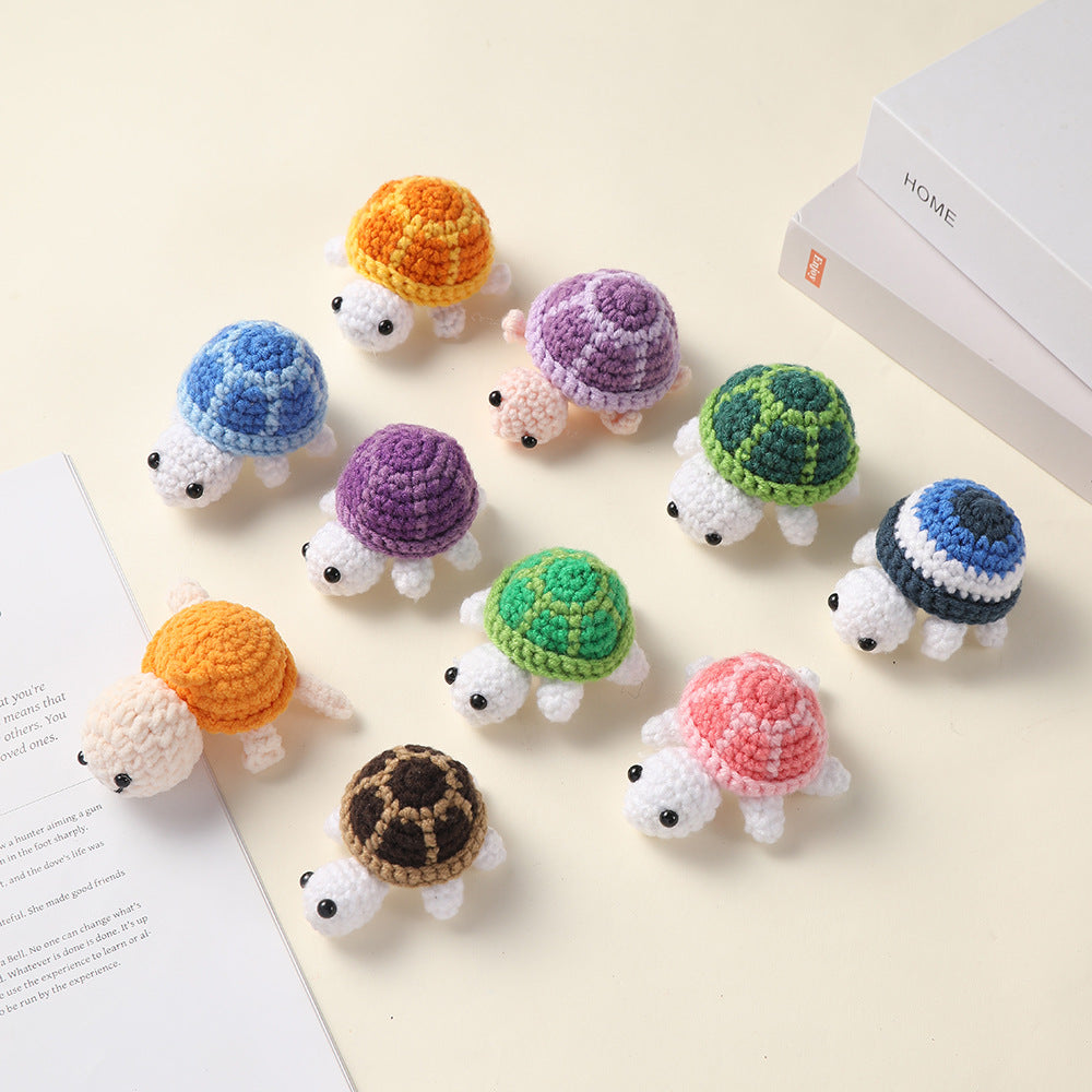 Ten small crocheted turtles in different shell colors scattered on a cream surface with books