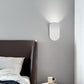 White curved wall lamp above a dark leather headboard with light washing up the grey wall