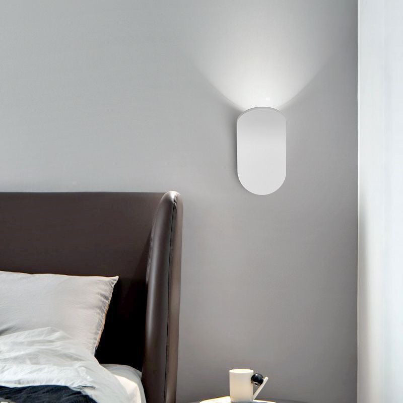 White curved wall lamp above a dark leather headboard with light washing up the grey wall