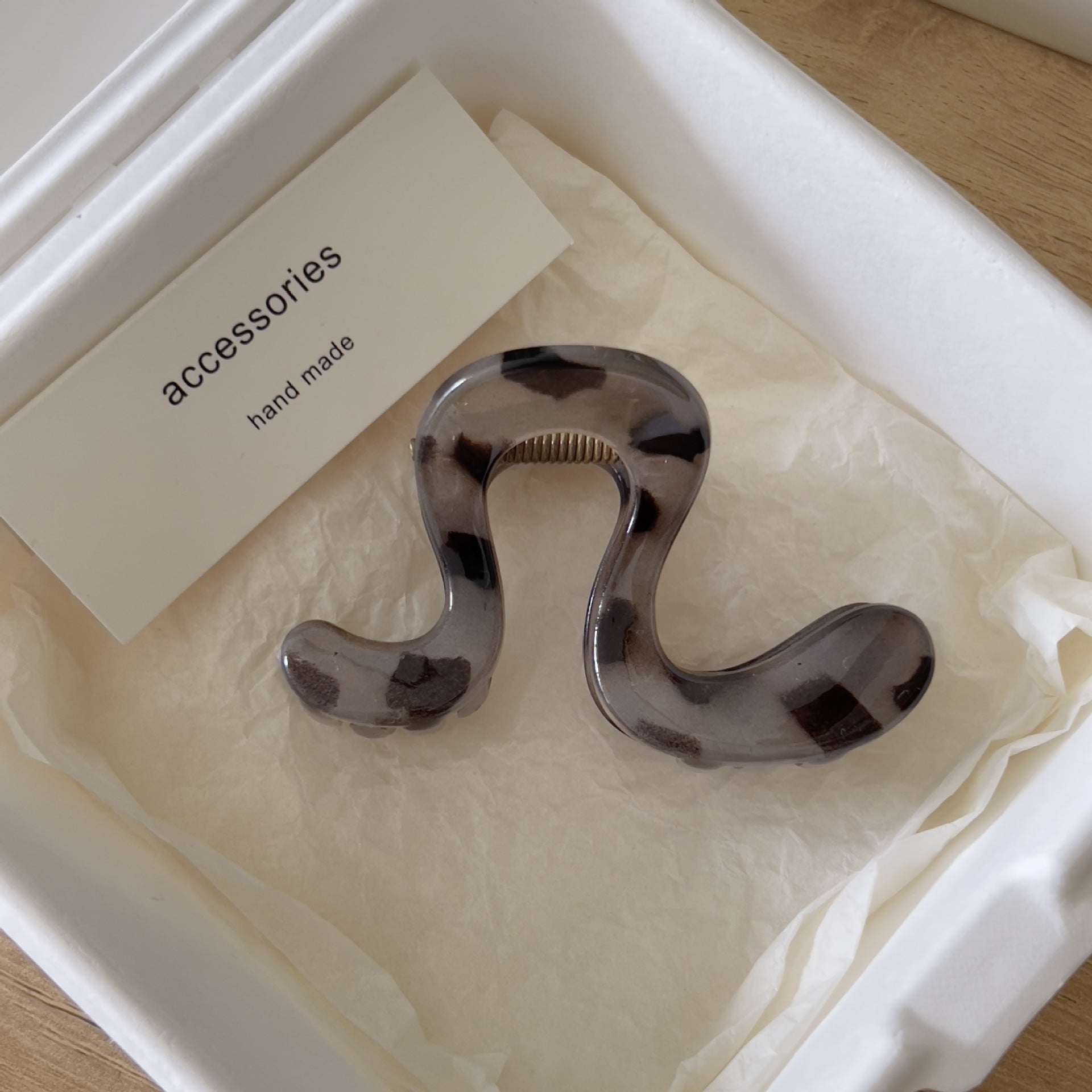 Large acrylic hair claw clip in a soft wavy shape displayed on cream paper