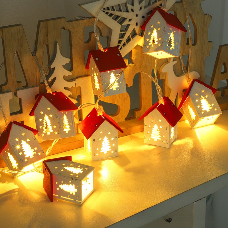 White wooden house string lights with tree cut-outs glowing warm white on a shelf beside festive letters