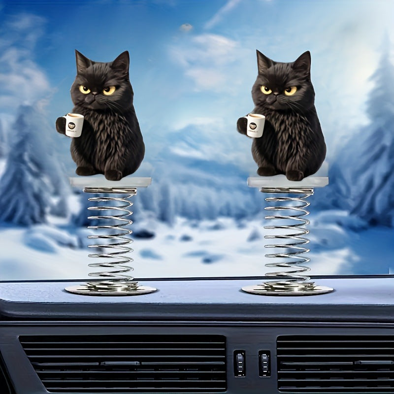 Two black cat spring ornaments on a car dashboard against a snowy mountain scene