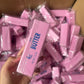 Hand holding a pink butter stick squishy toy in a clear bag above a box of pink sticks