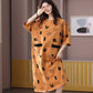 Woman covering her eyes in an orange short sleeve nightgown with black shapes and black trim at the hip, view 5 of 7