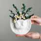 Hands holding the white ceramic cowboy hat vase, showing the embossed brim relief