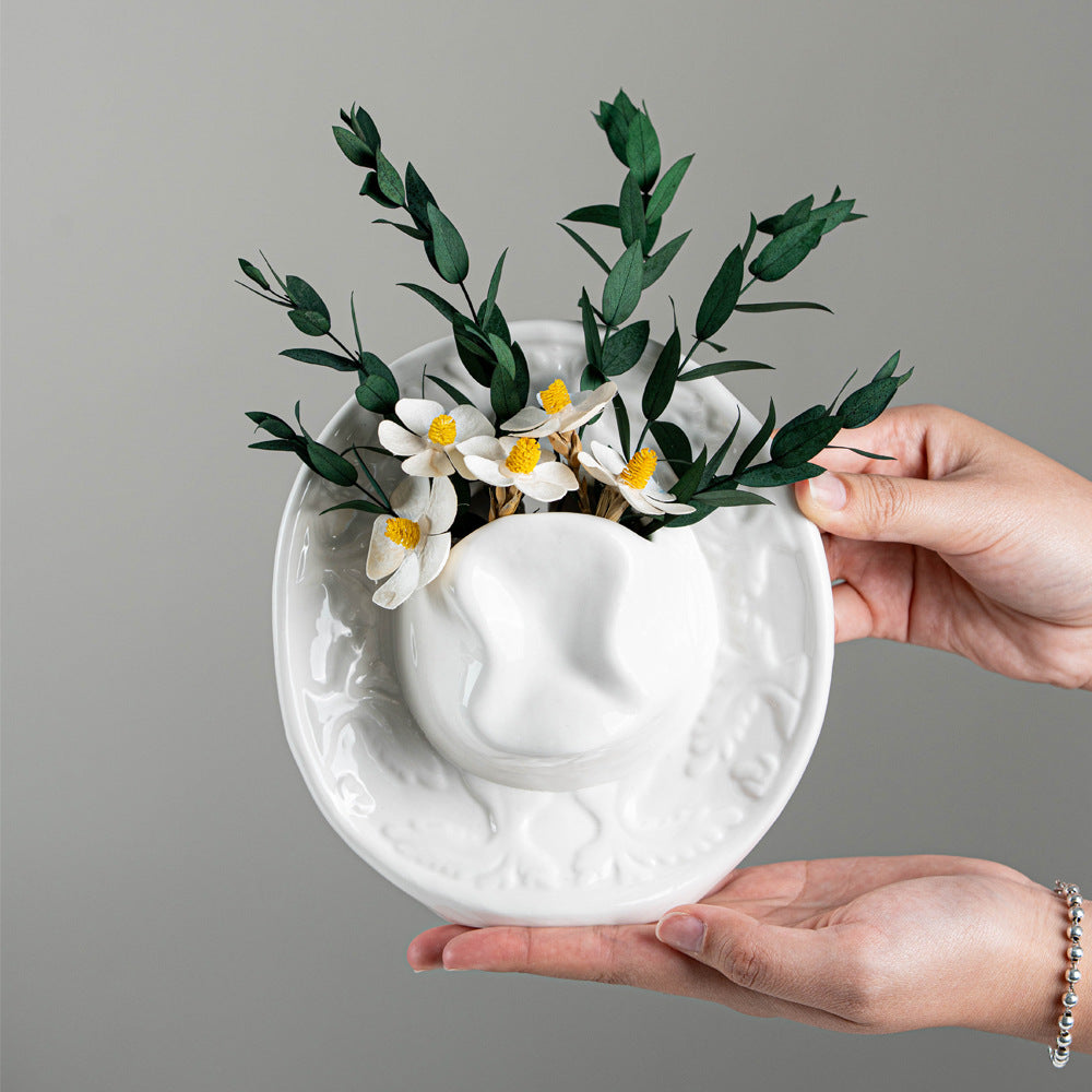 Hands holding the white ceramic cowboy hat vase, showing the embossed brim relief
