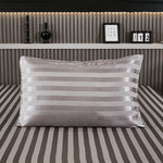Dark gray stripe satin pillowcase on a bed with matching striped sheets
