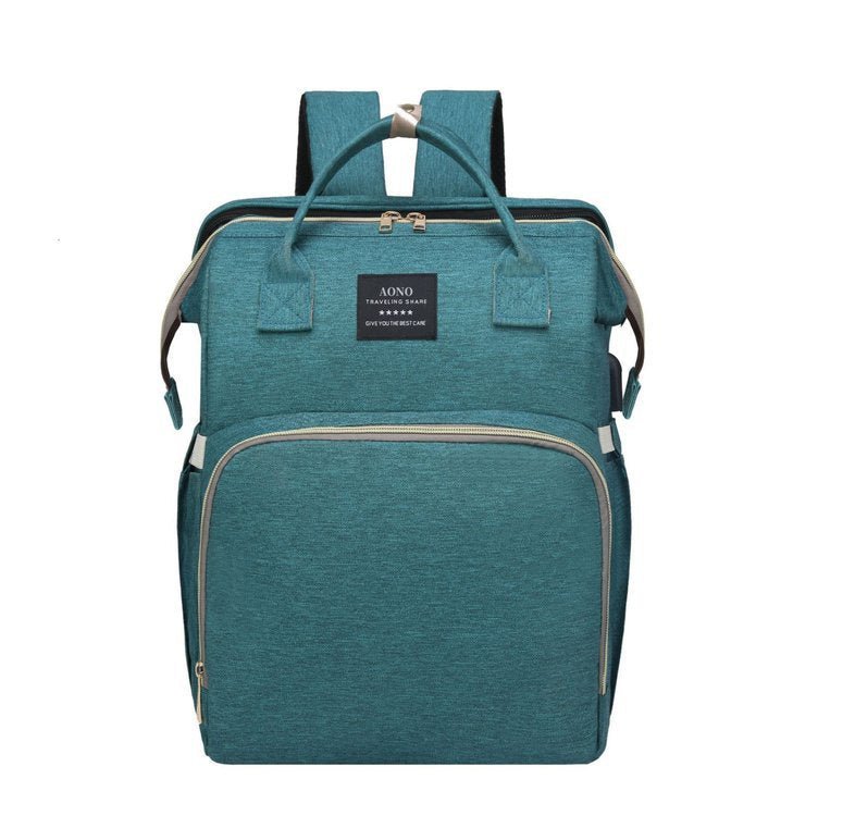 Green diaper backpack in a teal tone, front view with two top handles, a woven label and a front zip pocket