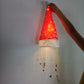 Hand holding a red hat light that glows red above strands of hanging charms against a plain wall