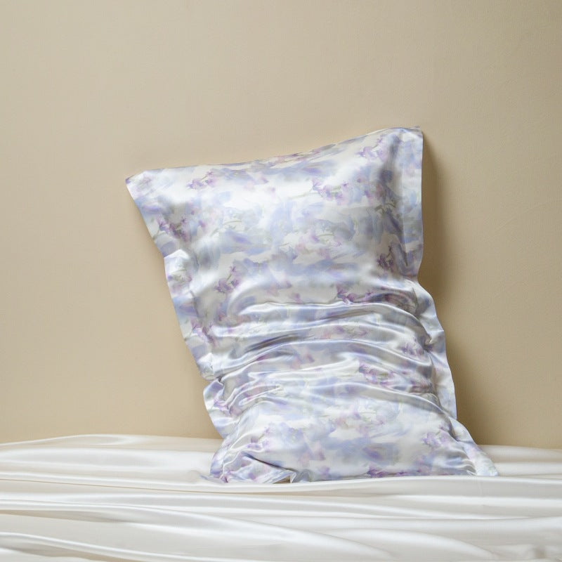 Lilac and white watercolor print silk pillowcase leaning on a beige wall above white silk