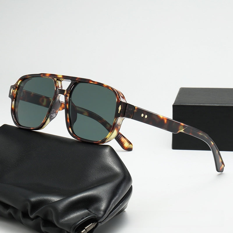 Square double bridge sunglasses with a tortoise frame and green lenses on a black case